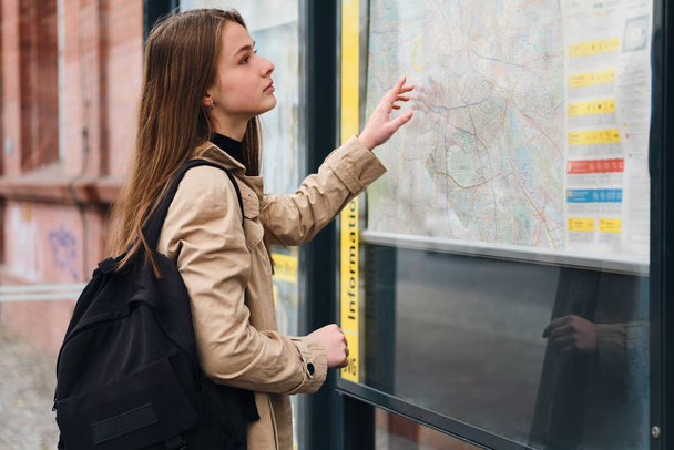 Atrakcyjny casual dziewczyna z plecakiem patrząc na mapę miasta na przystanku autobusowym outdoor - Zdjęcie, obraz