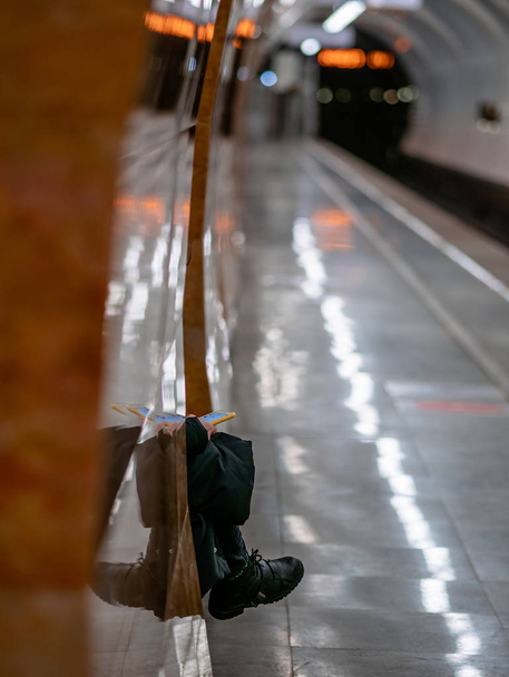 Felismerhetetlen metró utas várja a vonatot egy mobiltelefonnal a kezében. Egy nő ül egy padon egy metró peronon várja a metró autó Moszkvában metró télen ruházat - Fotó, kép