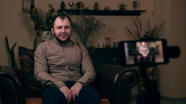 Ο σημαίνων Γενειοφόρος Νεαρός, ένας blogger, ευρωπαϊκής εμφάνισης, κάθεται σε μια καρέκλα φορώντας ένα πουκάμισο και καταγράφει ένα video vlog. Έννοια Blogging Social Media. - Πλάνα, βίντεο