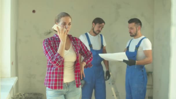 Woman records a voice message, repairmen stands on the background - Footage, Video