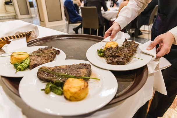 Camarero recoge un plato con un filete de carne durante una cena en un r
 - Foto, Imagen