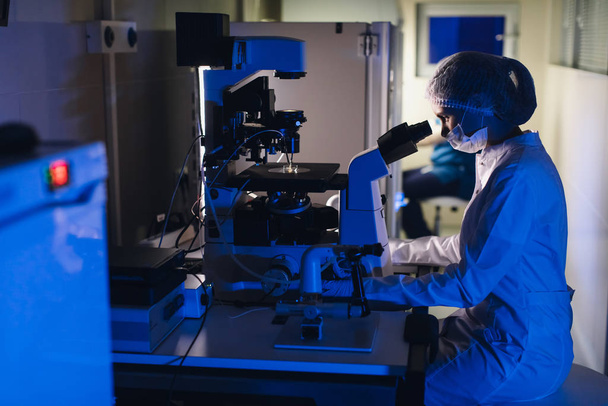 Σε ένα σύγχρονο εργαστήριο Επιστήμονας διεξαγωγή πειραμάτων. Ο εμβρυολόγος εξετάζει δείγματα με μικροσκόπιο - Φωτογραφία, εικόνα