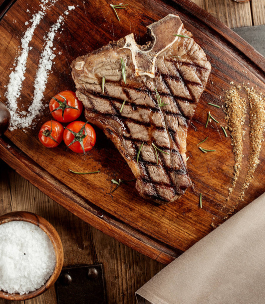 grilled t-bone steak served with salt herbs and grilled cherry tomatoes - Foto, Bild