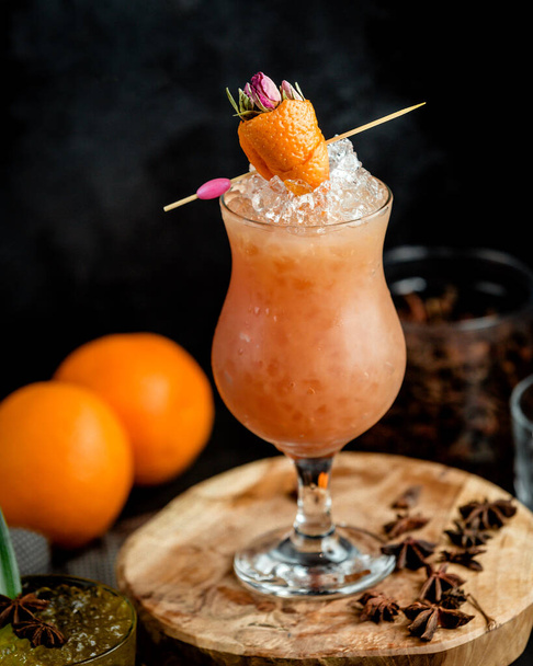 a glass of iced orange cocktail garnished with orange zest in strawberry shape - Фото, изображение