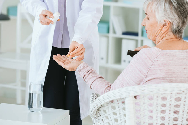 Γυναίκα γιατρός που δίνει σε ηλικιωμένη γυναίκα που πάσχει από το σύνδρομο Parkinson χάπια στην κλινική - Φωτογραφία, εικόνα