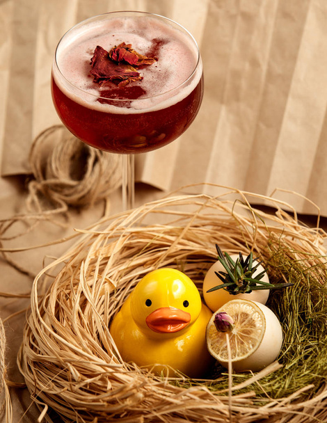 red cocktail garnished with dried rose petals next to ceramic yellow duckling - Photo, image