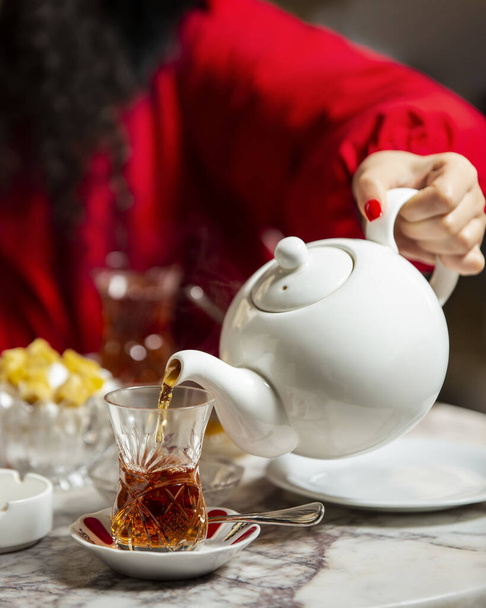 woman pouring black tea from teapot into armudu glass - Valokuva, kuva