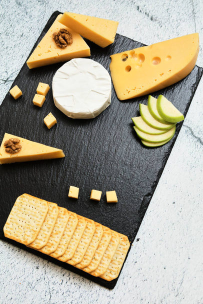 Pieces of cheese on a dark background. Cheeseboard. Sliced apple and nuts on the board.  - Fotoğraf, Görsel