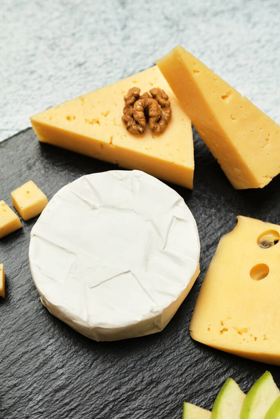 Pieces of cheese on a dark background. Cheeseboard. Sliced apple and nuts on the board.  - 写真・画像