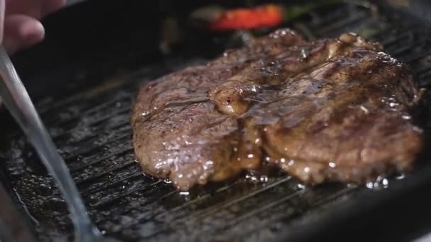 mannelijke kok giet geurige olie op een stuk marmeren biefstuk op een grill pan. Gefrituurde biefstuk in een restaurant. het bereiden van voedseldelen in de keuken. Kook recepten. heerlijk eten voor fijnproevers. close-up - Video