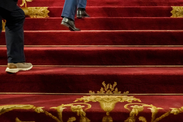 Detalle de personas subiendo una elegante escalera con alfombra roja
,  - Foto, imagen