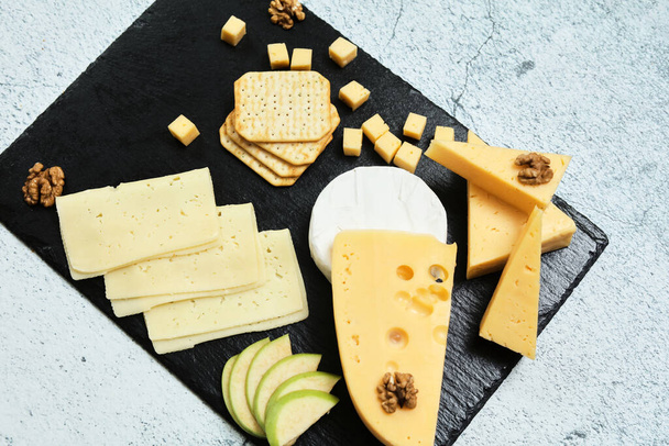 Pieces of cheese on a dark background. Cheeseboard. Sliced apple and nuts on the board.  - Foto, Imagen
