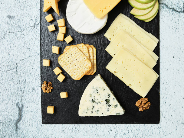 Pieces of cheese on a dark background. Cheeseboard. Sliced apple and nuts on the board.  - Zdjęcie, obraz