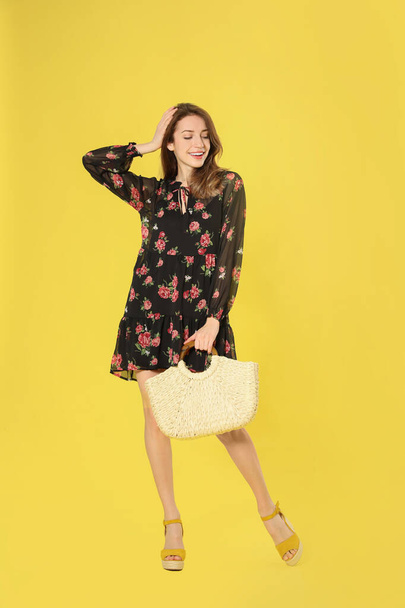 Young woman wearing floral print dress with straw bag on yellow  - 写真・画像