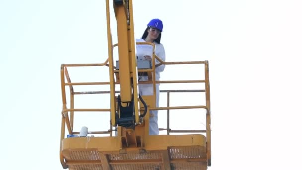 La mujer con equipo de seguridad baja la plataforma de un elevador telescópico de brazo usando el panel de control en cámara lenta. Concepto de trabajo
. - Imágenes, Vídeo