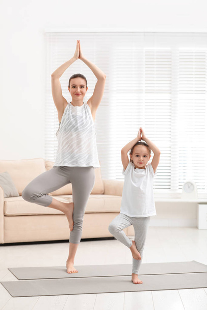 Jovem mãe com pequena filha praticando ioga em casa
 - Foto, Imagem
