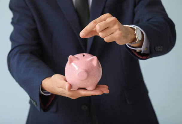 Male bank manager with piggy bank on light background, closeup - 写真・画像