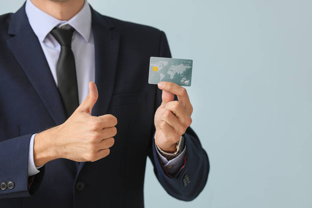 Male bank manager with credit card showing thumb-up gesture on light background - Foto, afbeelding