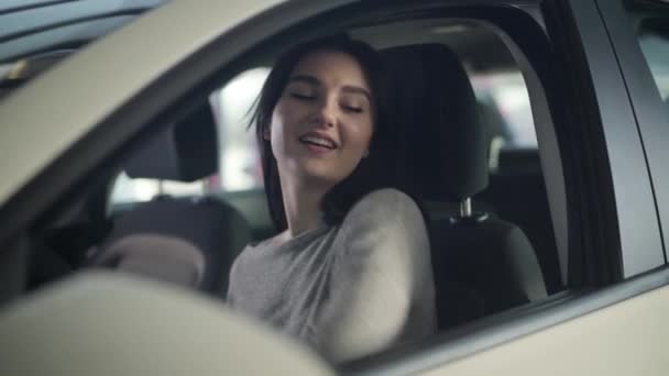 Portrait of young attractive Caucasian woman looking at camera as sitting on drivers seat in new car. Happy successful businesswoman posing in her automobile in dealership. Lifestyle, joy, happiness. - Кадри, відео