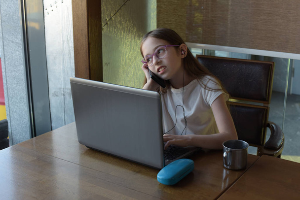 Nuori viehättävä nainen käyttää kannettavaa tietokonetta istuessaan moderni kahvila sisustus. Tyttö ja kannettava tietokone
. - Valokuva, kuva