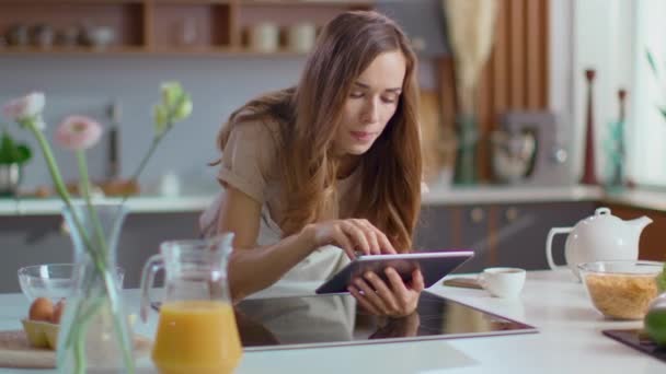 Attractive woman using digital tablet on kitchen. Girl browsing internet on pad - Filmmaterial, Video