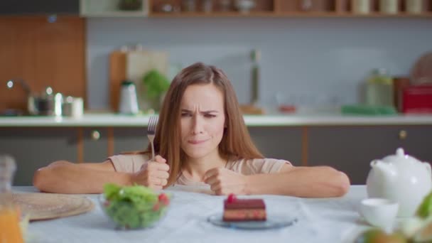Mulher escolhendo salada em vez de bolo na cozinha. Menina com garfo tentando salada fresca
 - Filmagem, Vídeo