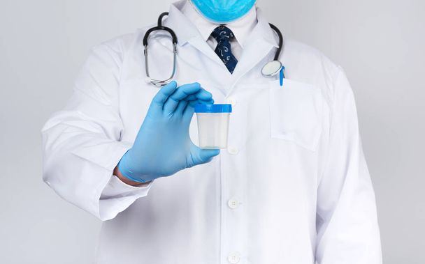 mannelijke arts in een witte jas en stropdas staat en houdt een plastic c - Foto, afbeelding