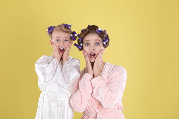 Emotional mother and daughter with curlers on yellow background - Φωτογραφία, εικόνα