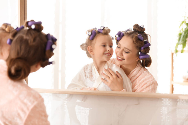 Happy mother and daughter with curlers near mirror in bathroom - Фото, зображення