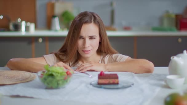 Attractive woman choosing between salad and cake on table. Healthy food concept - Video