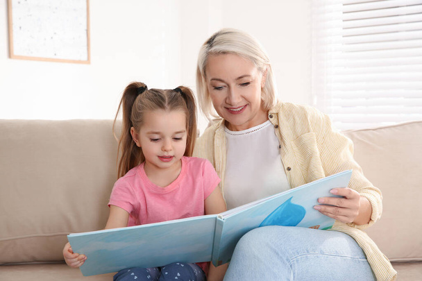 Mature woman with her little granddaughter reading book together - Foto, Bild
