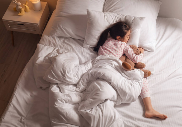 Χαριτωμένο κοριτσάκι από την Ασία κοιμάται στο κρεβάτι - Φωτογραφία, εικόνα