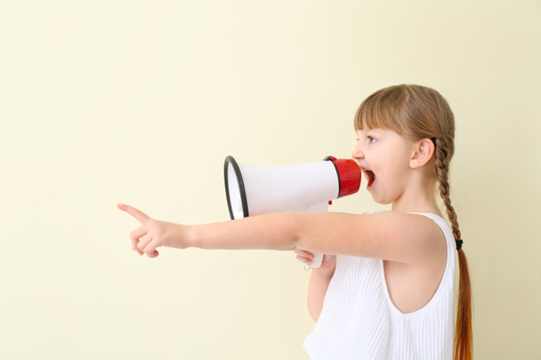 Cute little girl with megaphone pointing at something on light background - Photo, image