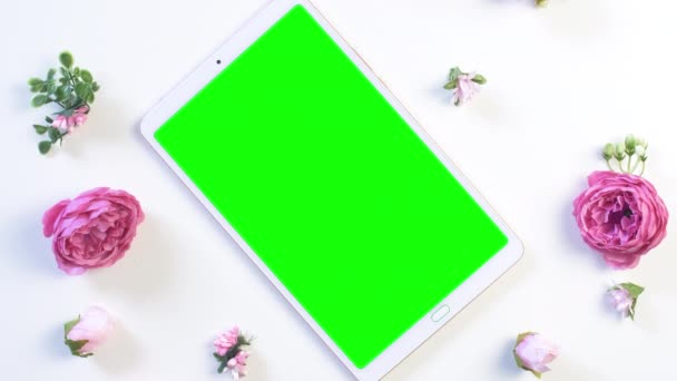 Bílá tableta se zelenou obrazovkou na stole s růžovou růžovou květinou. Letní nebo sprink pozadí záběry. Horní pohled. Záběry 4k.  - Záběry, video