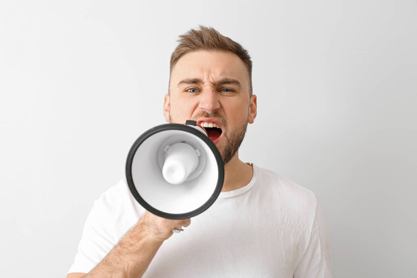 Emotional young man with megaphone on light background - Photo, Image