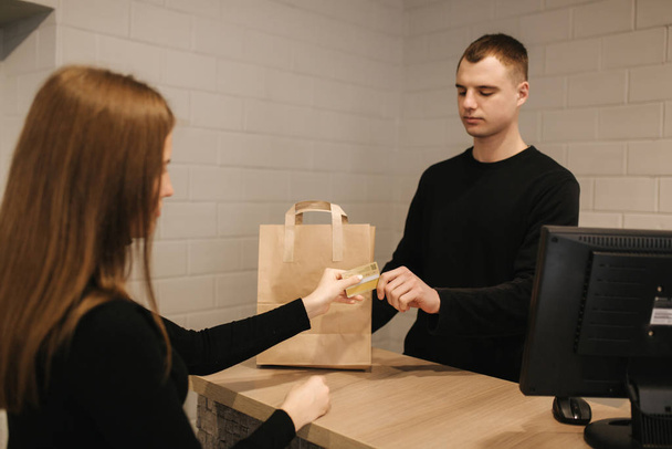 Attractive woman is giving a credit card to shop manager. Customer give credit card to assistant and smiling while doing shopping in boutique - Valokuva, kuva