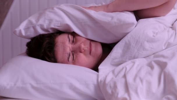 Frau versucht zu schlafen, genervt von schlechten lauten Zimmernachbarn, die Ohren mit Kissen bedecken, wacht im Bett liegend auf und leidet unter Schlaflosigkeit - Filmmaterial, Video