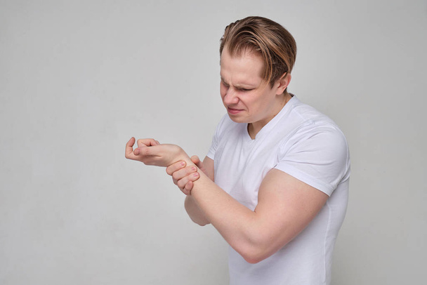 Ein Mann im weißen T-Shirt massiert sein Handgelenk nach einer Prellung und einer Fraktur. - Foto, Bild