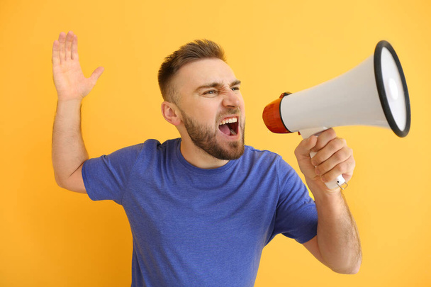 Emotional young man with megaphone on color background - Photo, Image