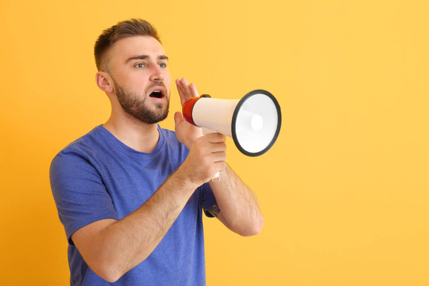 Emotional young man with megaphone on color background - Foto, Bild