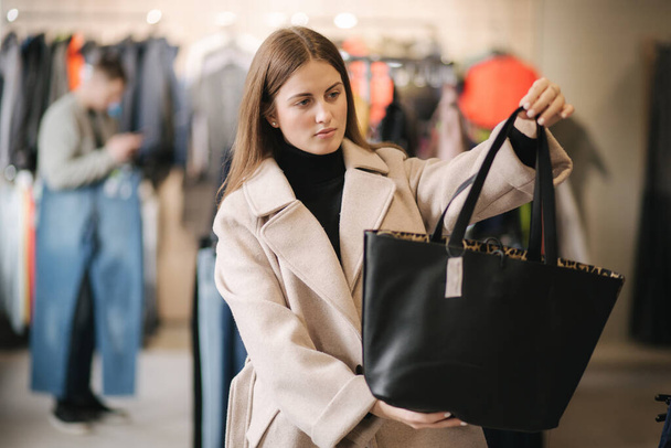 Mladá žena si zkouší černou tašku. Žena v butiku - Fotografie, Obrázek