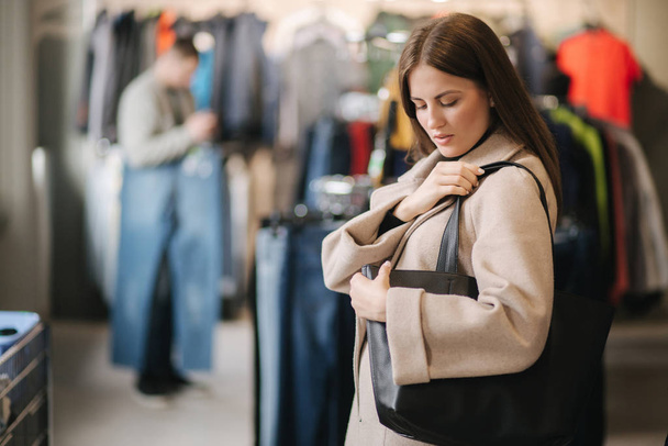 Young woman trying on black bag. Woman in boutique - 写真・画像