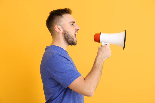 Emotional young man with megaphone on color background - Foto, imagen