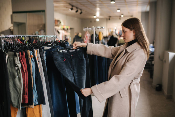Молода красива жінка шукає нові джинси в магазині одягу
 - Фото, зображення