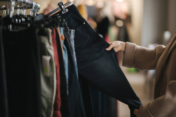 Close-up van de vrouw die jeans kiest. Hand van vrouwelijke holding jeans in kleding winkel - Foto, afbeelding