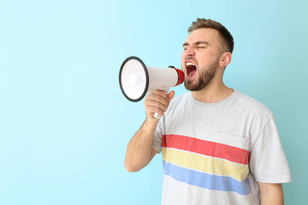 Emotional young man with megaphone on color background - 写真・画像
