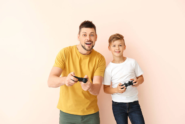 Father and his little son playing video games on color background - Фото, изображение