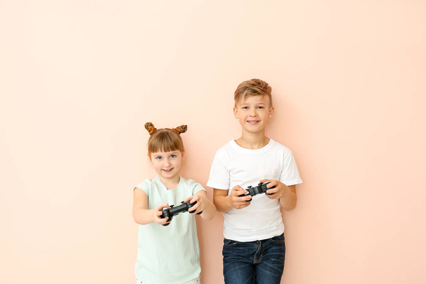Μικρά παιδιά που παίζουν βιντεοπαιχνίδια σε έγχρωμο φόντο - Φωτογραφία, εικόνα