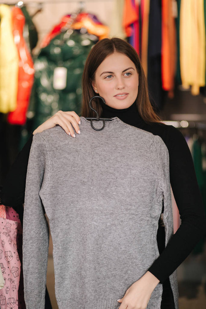 Chica atractiva Pruébate sudadera gris en la tienda de ropa
 - Foto, imagen