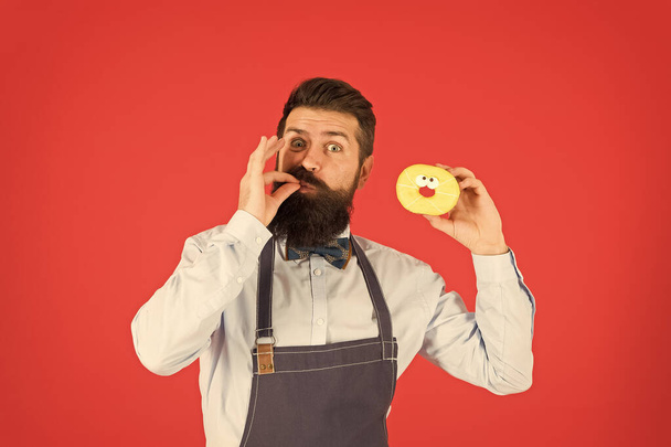 You will lick your fingers. Bearded man enjoying sweet taste of doughnut on red background. Baker eating donut with classic taste dessert. It tastes good. Come experience the taste of joy - Foto, Imagen